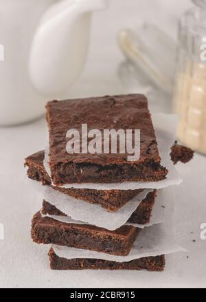 Una pila di brownie di cioccolato con carta pergamena tra posto su sfondo bianco. Delizioso dessert. Foto Stock