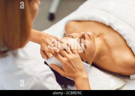 Concetto di bellezza e salute della pelle del viso. Una donna riceve un massaggio viso da un estetista clinica Foto Stock