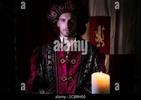 Ritratto di re attraente con barba vestita in costume alla macchina fotografica con la candela in primo piano Foto Stock