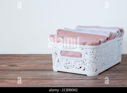 Contenitore bianco organizer con vestiti perfettamente ripiegati su tavolo di legno. Concetto di storage verticale compatto Foto Stock