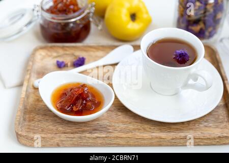 Marmellata di mele cotogne fatta in casa in una ciotola di porcellana con una tazza di tè su un vassoio di legno sullo sfondo è un vaso di vetro con marmellata e mela cotogna. Foto Stock