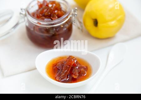 Marmellata di mele cotogne fatta in casa in una ciotola di porcellana con una tazza di tè. Sullo sfondo c'è un vaso di vetro con marmellata e mela cotogna. Foto Stock