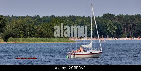 Gifhorn, Germania, 9 agosto 2020: Coppia di mezza età che si rilassa su una barca a vela tirando un materasso ad aria dietro di loro sul lago Foto Stock