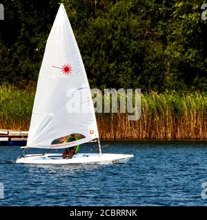 Gifhorn, Germania, 9 agosto 2020: Piccola agile barca a vela veloce che naviga nel lago di fronte alla cintura di canna Foto Stock