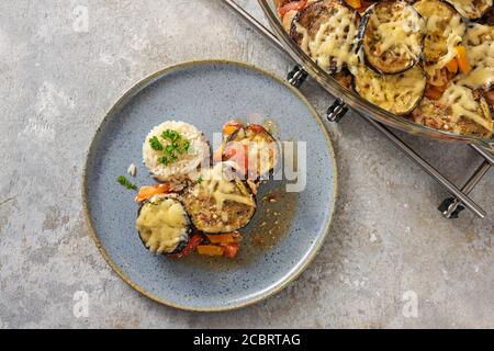 Casseruola fatta in casa di melanzane, pomodoro e peperone con riso su un piatto blu e uno sfondo grigio rustico, spazio copia, vista ad alto angolo da abov Foto Stock