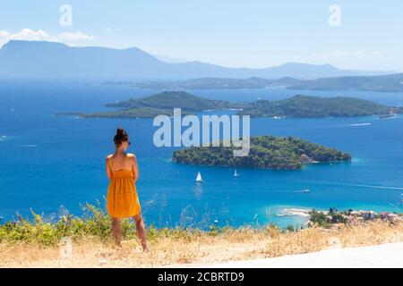 Una ragazza in abito giallo gode di una vista costiera da una strada sopra Nidri, Lefkada, Isole IONIE, Grecia Foto Stock