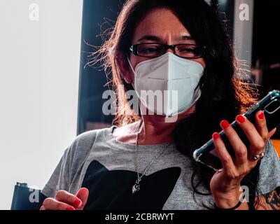 Brunette latina femmina indossatrice Rpotective fp2 viso maschera bianca lavorare in remoto in ufficio a casa Foto Stock