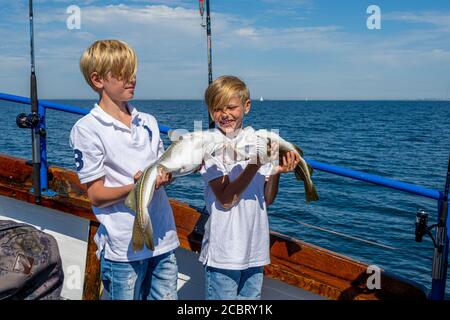 Malmo, Svezia - 6 agosto 2020: Due ragazzi in un viaggio di pesca con la famiglia mostrano la loro cattura fresca di merluzzo. Oceano blu e cielo sullo sfondo Foto Stock