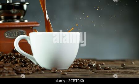 Versare il caffè circondato da chicchi di caffè e mulino. Closeup di annata natura morta Foto Stock