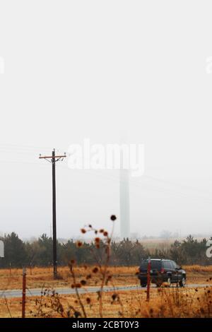 Strada in Okalhoma con base di turbina eolica visibile attraverso La nebbia Foto Stock