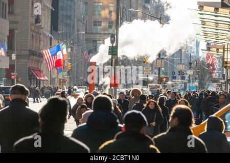 Una folla di persone cammina lungo la Midtown Fifth Avenue sotto il vapore che si sposta. Foto Stock