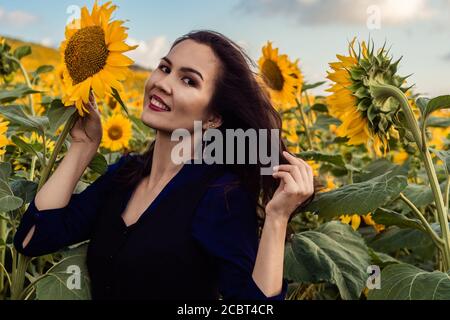 Ragazza asiatica è circondata da girasoli e sorridente. Campo con girasoli sullo sfondo. Foto Stock