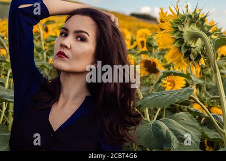 Ragazza asiatica è circondata da girasoli e sorridente. Campo con girasoli sullo sfondo. Foto Stock