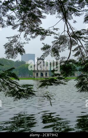 Hanoi, Vietnam, lago Hoan Kiem con la Torre delle tartarughe (pagoda) incorniciata tra le foglie. Riflessione in un'immagine HDR verticale. Foto Stock