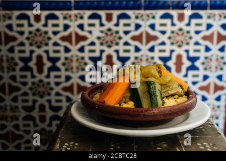 Delizioso couscous con carote e verdure, in tajine, su rustico tavolo in legno e tradizionali piastrelle arabe sullo sfondo Foto Stock