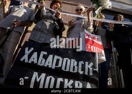 Mosca, Russia. 15 agosto 2020 le donne che tengono fiori e un nastro bianco, simbolo del movimento di opposizione, rimangono in una catena di solidarietà durante un raduno contro i risultati delle elezioni presidenziali bielorusse davanti all'ambasciata bielorussa a Mosca, Russia. La bandiera nera recita 'Khabarovsk - Mosca' a sostegno dei manifestanti nella regione russa di Khabarovsk Foto Stock