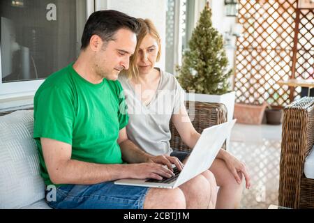 Coppia di mezza età che usa il computer portatile e divertirsi a casa al balcone. Un concetto di coppia con i giovani che si divertono insieme Foto Stock