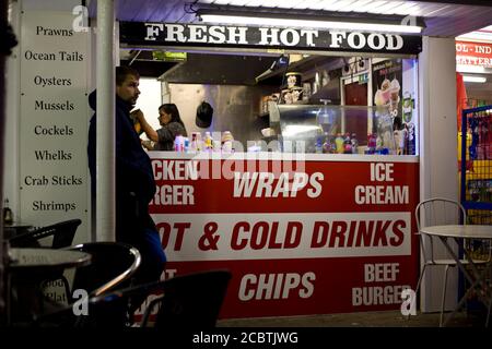 Uomo in attesa fuori di un fornitore di strada take away. Scena gritty, mangiare a tarda notte, cibo caldo fresco, Blackpool Promenade, mangiare veloce, fotografia di strada, Foto Stock