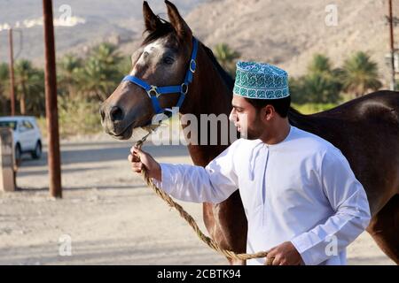 Un uomo omani che indossa cappellino tradizionale allenando il suo cavallo Foto Stock