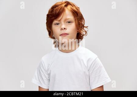 Un adolescente con testa rossa in una t-shirt bianca guarda in avanti uno sfondo grigio Foto Stock