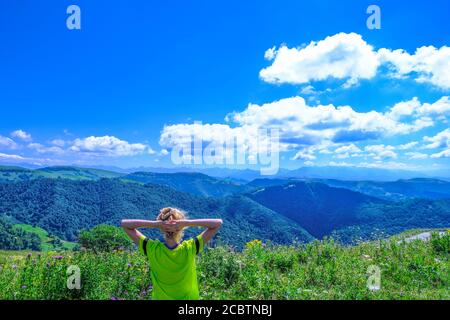 giovane turista che alza le mani e gode di una vista fantastica sulla natura, la foresta e le montagne alpine. Paesaggio montuoso Foto Stock