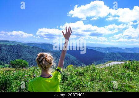 giovane turista che alza le mani e gode di una vista fantastica sulla natura, la foresta e le montagne alpine. Paesaggio montuoso Foto Stock