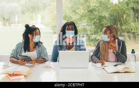 Tre alunni afro-americani seduti al tavolo che si preparano per l'esame o che fanno i compiti insieme, stanno usando il lap top e il tablet digitale w Foto Stock