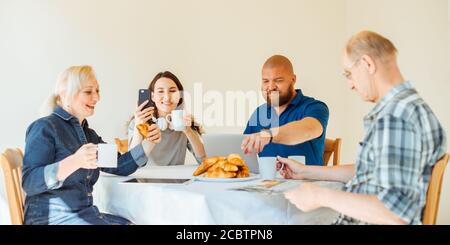 Felice famiglia multi generazionale leggere notizie al mattino mentre colazione Foto Stock