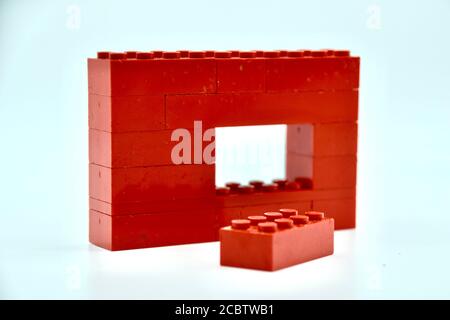 Concept studio immagine di una parete di mattoni rossi Lego sfondo bianco con uno spazio e un singolo mattone verso l'esterno la parte anteriore simboleggiando l'individualismo Foto Stock
