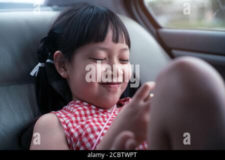 Bambina asiatica che gioca con smartphone in auto Foto Stock