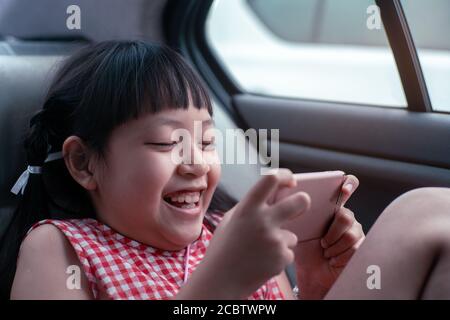 Bambina asiatica che gioca con smartphone in auto Foto Stock