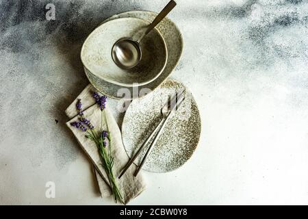 Tavolo estivo con posate e gres minimalistici serviti su fondo di cemento e decorato con fiori freschi di lavanda Foto Stock