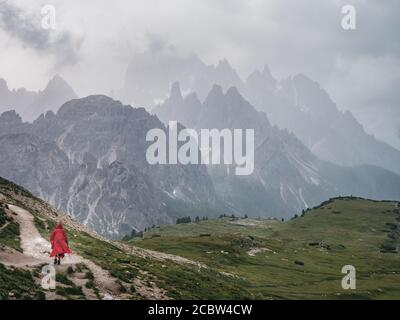 Escursionista in un poncho rosso camminando nel suggestivo paesaggio del parco nazionale delle tre Cime nelle Dolomiti, con le cime frastagliate del monte Cadini di Misurina gr Foto Stock