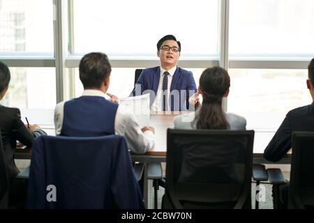 troppo fiducioso giovane uomo d'affari asiatico che parla grande di fronte di intervistatori di ore durante il colloquio di lavoro Foto Stock