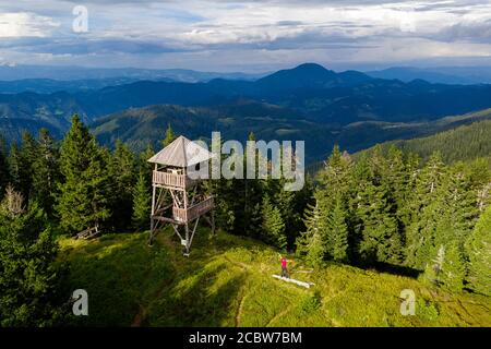 Donna con uno zaino in piedi su una panchina alla torre di osservazione su una montagna, vista aerea Foto Stock