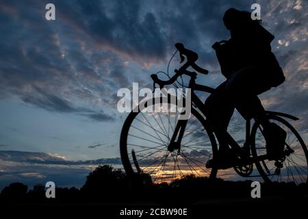 Un ciclista corre senza mani sul manubrio Un parco londinese al tramonto Foto Stock