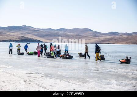 Un gruppo di turisti con le slitte di ghiaccio che camminano sulla superficie congelata del Lago Baikal, Russia Foto Stock