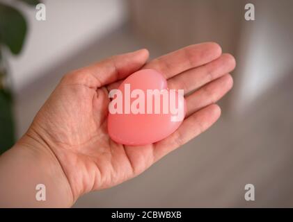 una donna tiene in mano un sapone a forma di cuore. Cuore simbolo di amore. Cuore rosa Foto Stock