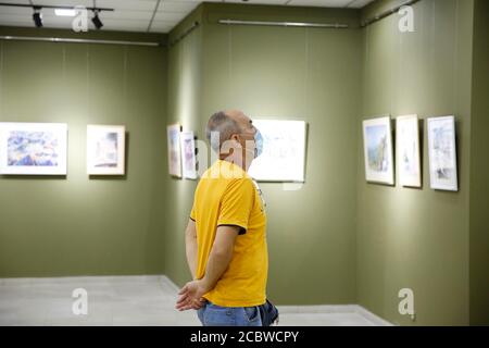 Bishkek, Kirghizistan. 15 agosto 2020. Un visitatore che indossa una maschera facciale ammira i dipinti dell'artista Emil Nasritdinov durante una mostra alla galleria del Parco Dubovy a Bishkek, Kirghizistan, 15 agosto 2020. Tutti i proventi della mostra saranno devoluti all'Associazione Fulbright Alumni per combattere contro COVID-19. Credit: Roman/Xinhua/Alamy Live News Foto Stock