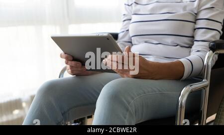 Donna di mezza età in sedia a rotelle con computer tablet. Foto Stock