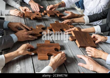 Il team di persone di affari seduti intorno al tavolo di riunione e l'assemblaggio di pezzi di puzzle di legno di cooperazione unità idee concetto Foto Stock
