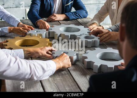 Gruppo di uomini d'affari che si uniscono a ingranaggi color argento e oro sul tavolo sul luogo di lavoro Foto Stock