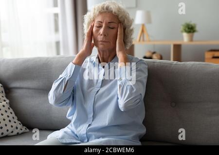 Malsana preoccupata vecchia donna matura massaggiando templi. Foto Stock