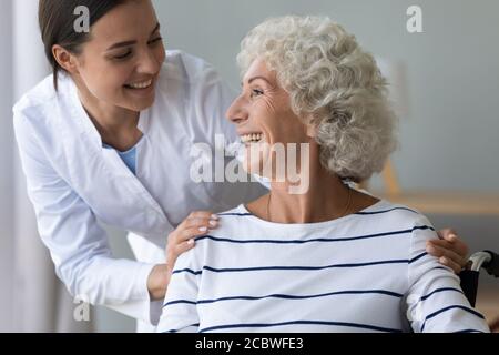 Sorridente giovane operaio medico che sostiene felice vecchia donna handicappata. Foto Stock