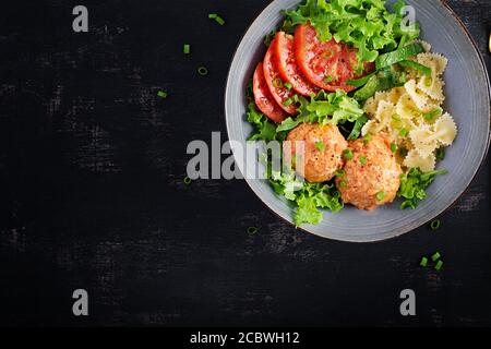 Pasta italiana. FARFALLE con polpette e insalata su sfondo scuro. Cena. Vista dall'alto, dall'alto. Concetto di cibo lento Foto Stock