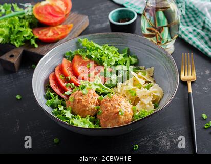 Pasta italiana. FARFALLE con polpette e insalata su sfondo scuro. Cena. Concetto di cibo lento Foto Stock