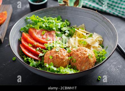 Pasta italiana. FARFALLE con polpette e insalata su sfondo scuro. Cena. Concetto di cibo lento Foto Stock