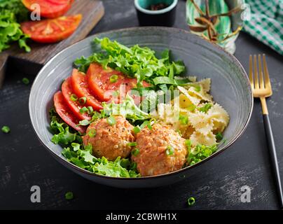 Pasta italiana. FARFALLE con polpette e insalata su sfondo scuro. Cena. Concetto di cibo lento Foto Stock