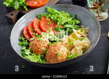 Pasta italiana. FARFALLE con polpette e insalata su sfondo scuro. Cena. Concetto di cibo lento Foto Stock