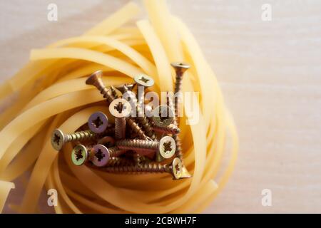 Le viti giacciono nel nido di spaghetti di fondo leggero Foto Stock